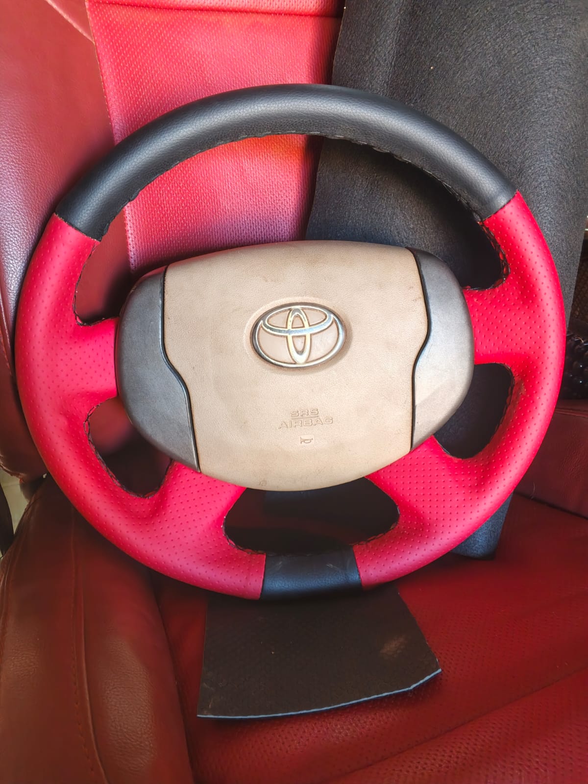 Red and black leather steering wheel cover fitted on a Toyota wheel