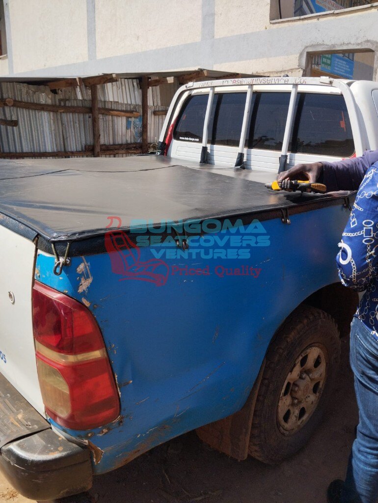 Installing a black flat bed cover on a Toyota Hilux pickup at Bungoma Seatcovers Ventures workshop